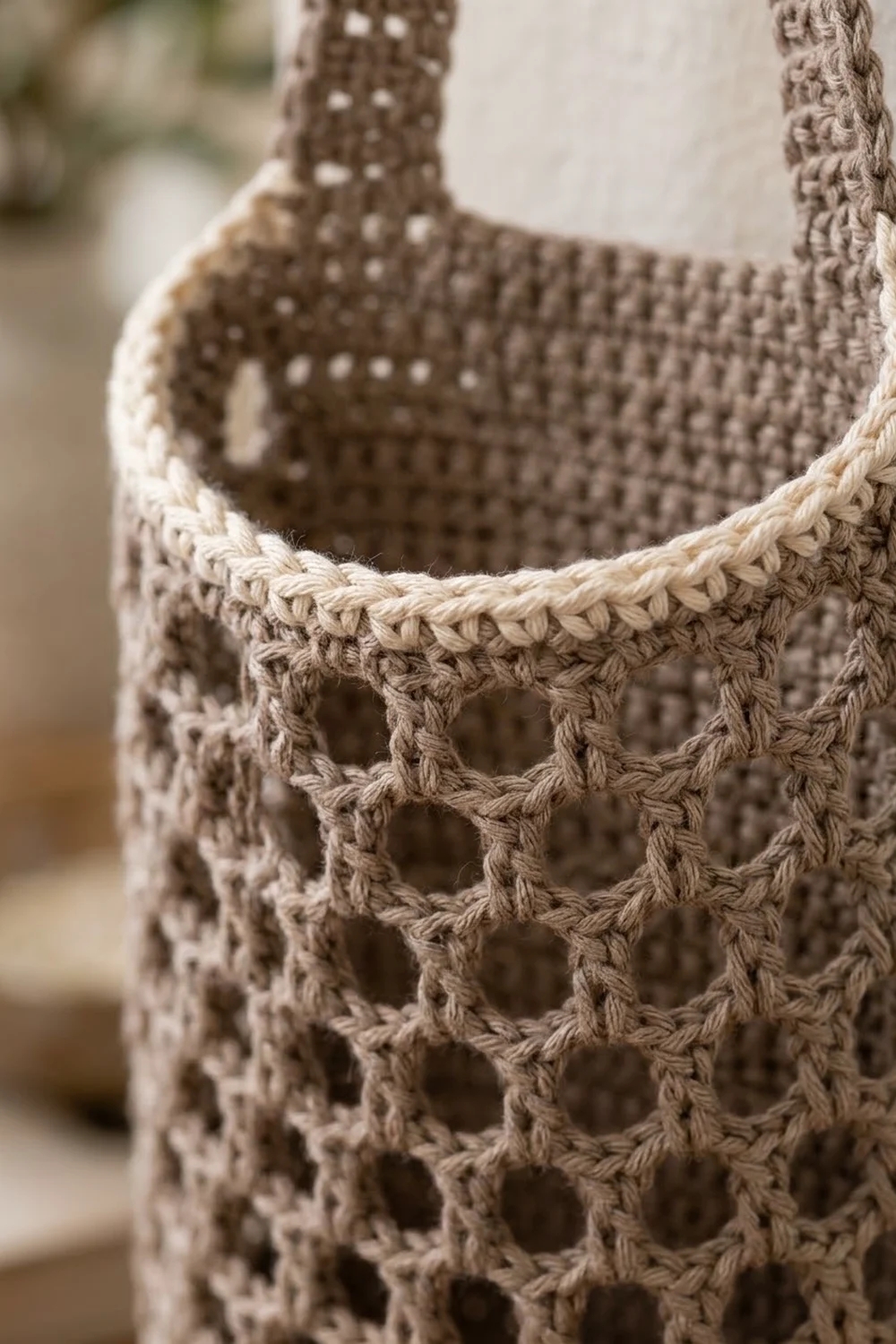 Close-up of a crocheted mesh basket in beige tones with open-work stitching and rope handles.
