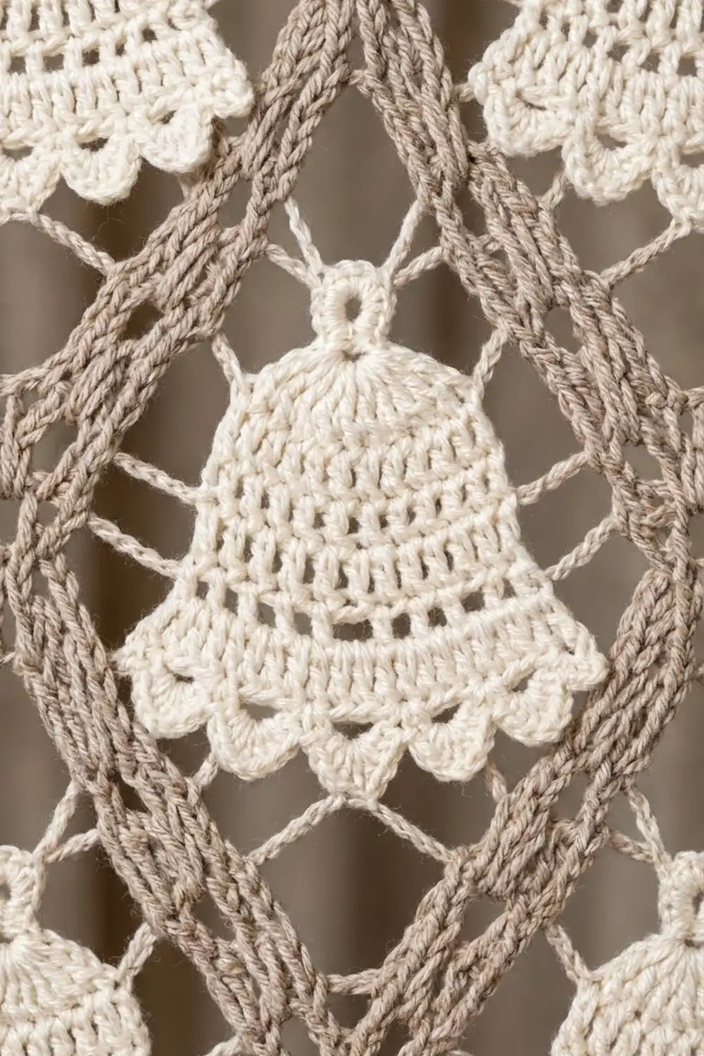 Cream-crocheted bell ornament with delicate lace detailing and scalloped edges, framed by twisted beige rope.