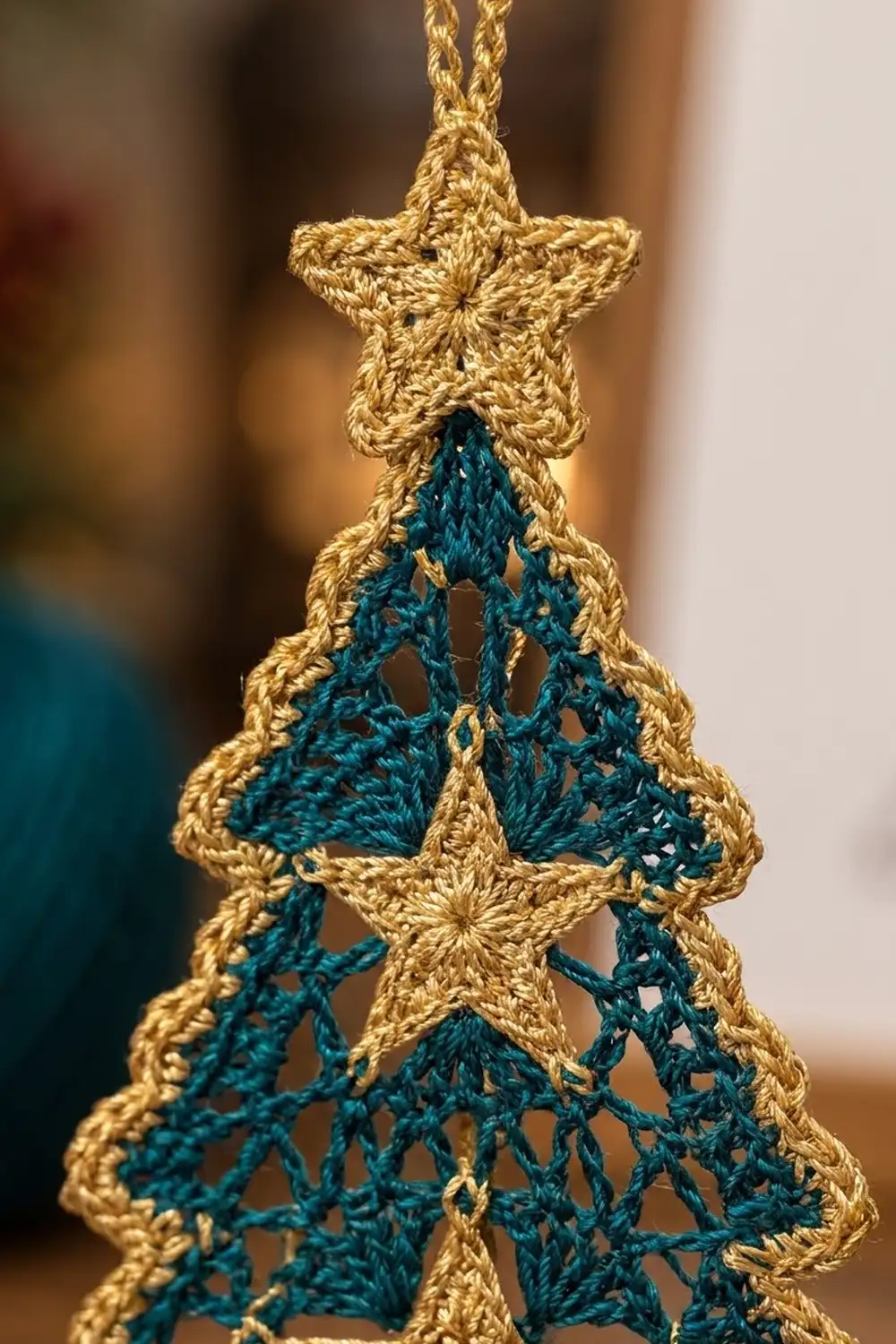 Gold-bordered crocheted Christmas tree ornament with delicate teal lace interior, hanging against a soft blurred background.