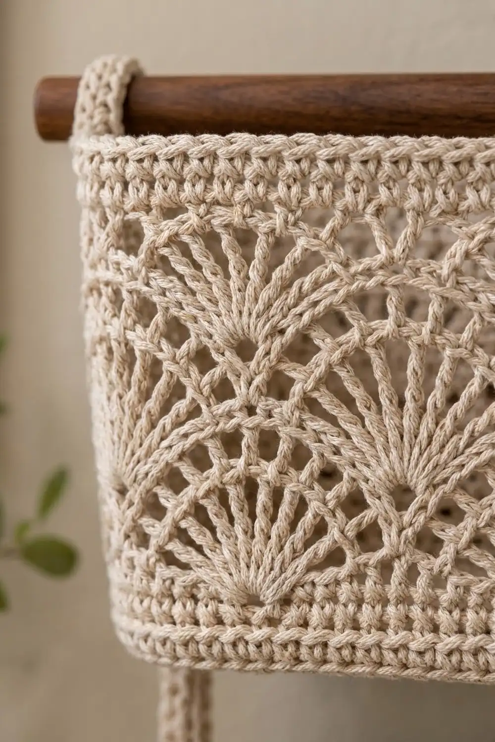 Cream-colored crochet with open geometric patterning draped over a dark wood dowel against a soft neutral background.