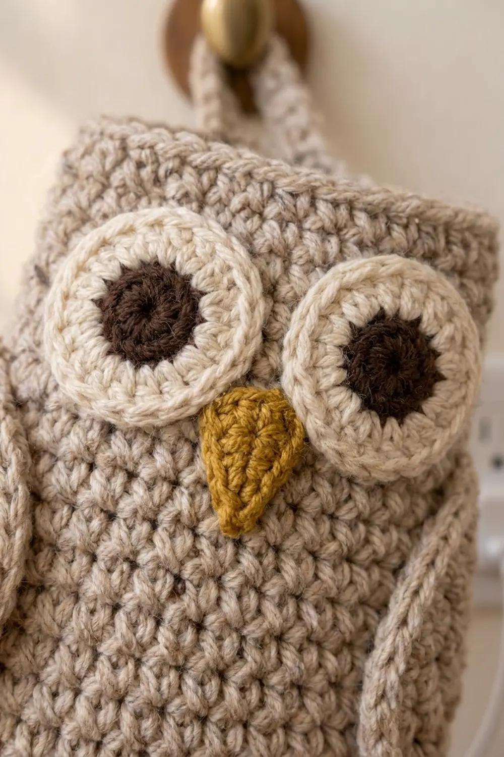 Detailed close-up of cream crocheted owl featuring white eyes with dark pupils and small golden beak.