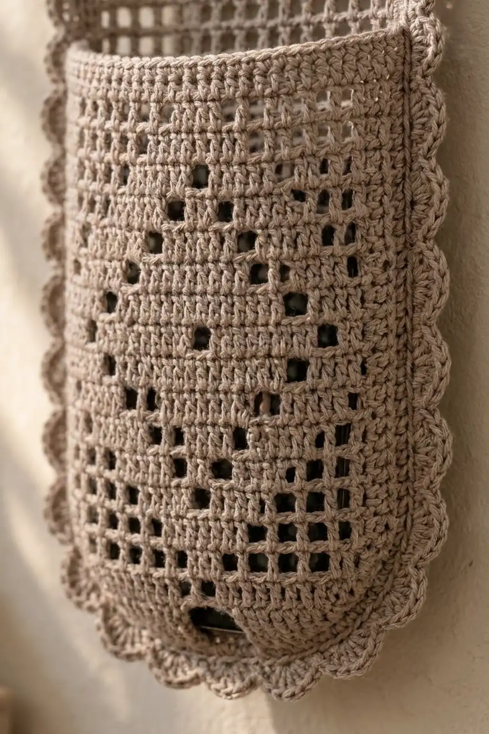 Closeup of beige crocheted lace featuring a geometric grid of openings with decorative scalloped edges.