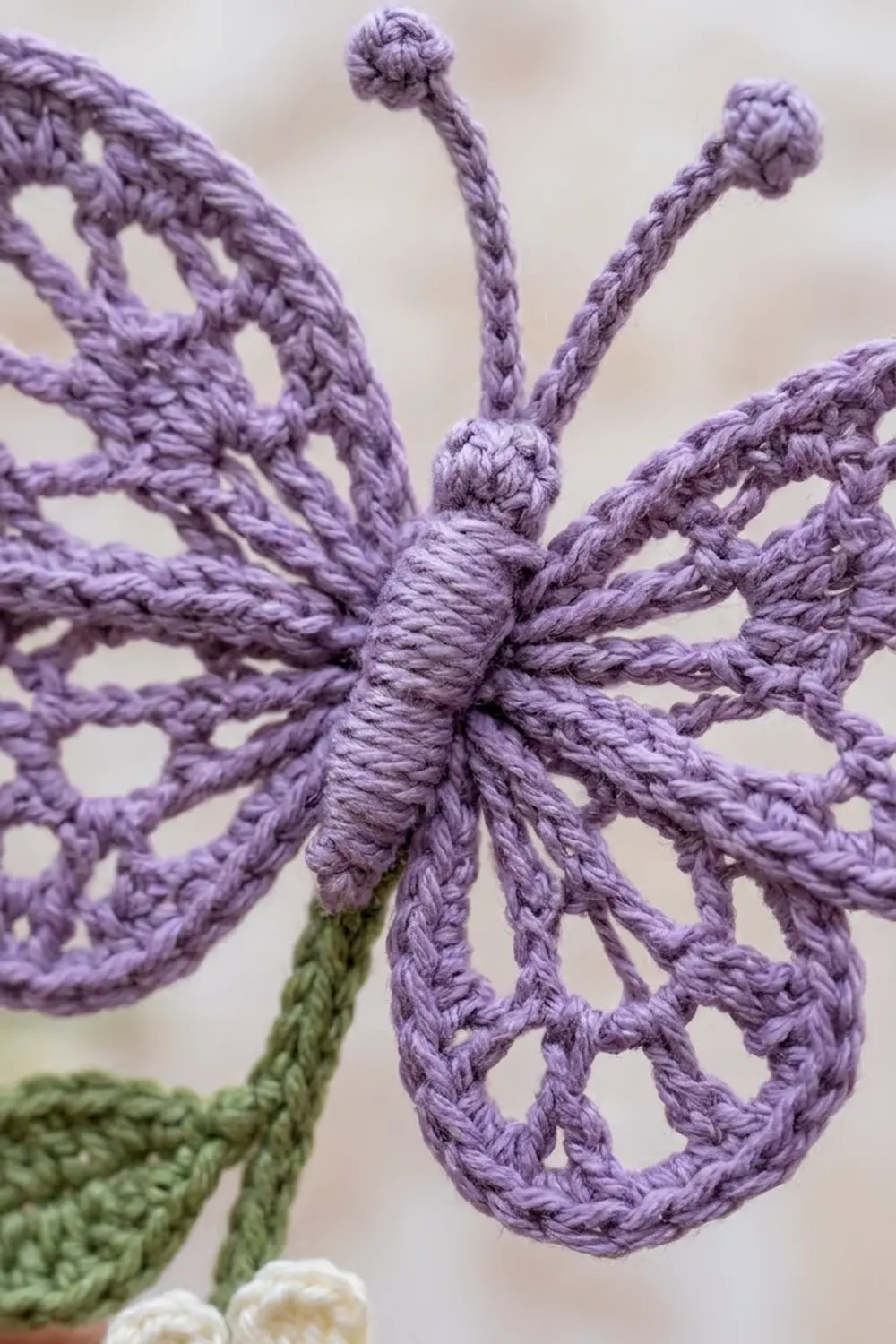 Purple crocheted flower with lacy open-work petals, wrapped center, pompom-tipped stamens, and green stem.