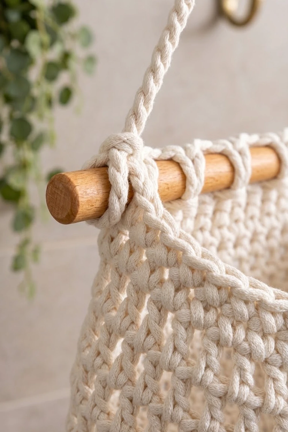 Close-up of cream-colored knotted rope wrapped around a wooden dowel in a textured macramé wall hanging.