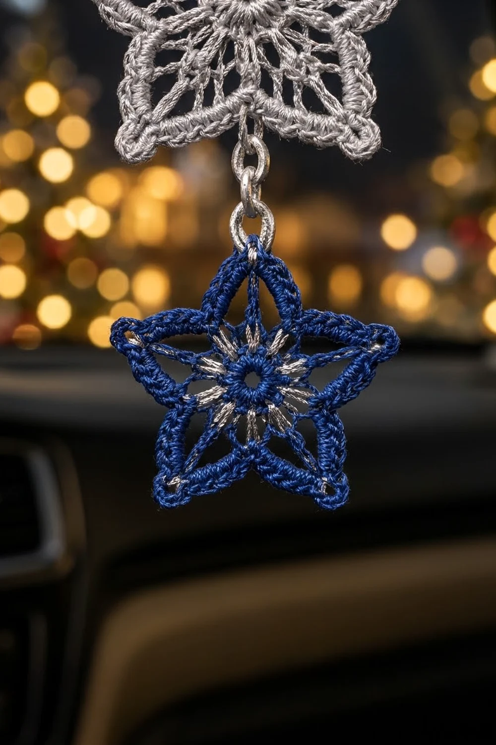 Handmade crocheted blue star ornament with silver centerpiece hanging from delicate white chain against golden bokeh background.