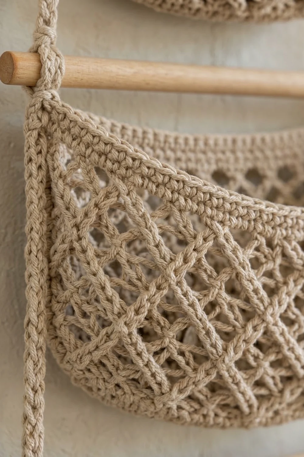 Detailed view of beige crocheted fabric with delicate openwork pattern hanging from a natural wooden rod.