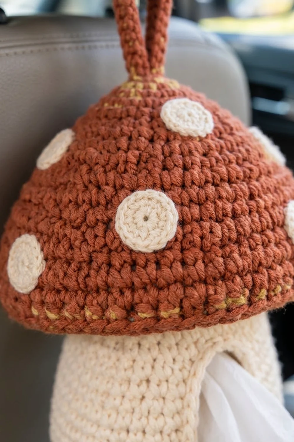 Crocheted mushroom with rust-red cap, white polka dots, cream stem, and yellow-edged base, showing detailed stitch work.