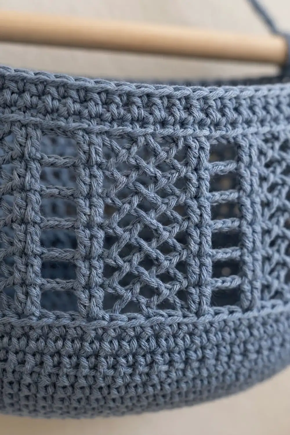 Close-up of blue-gray crocheted fabric with an open lattice pattern and wooden hook above.
