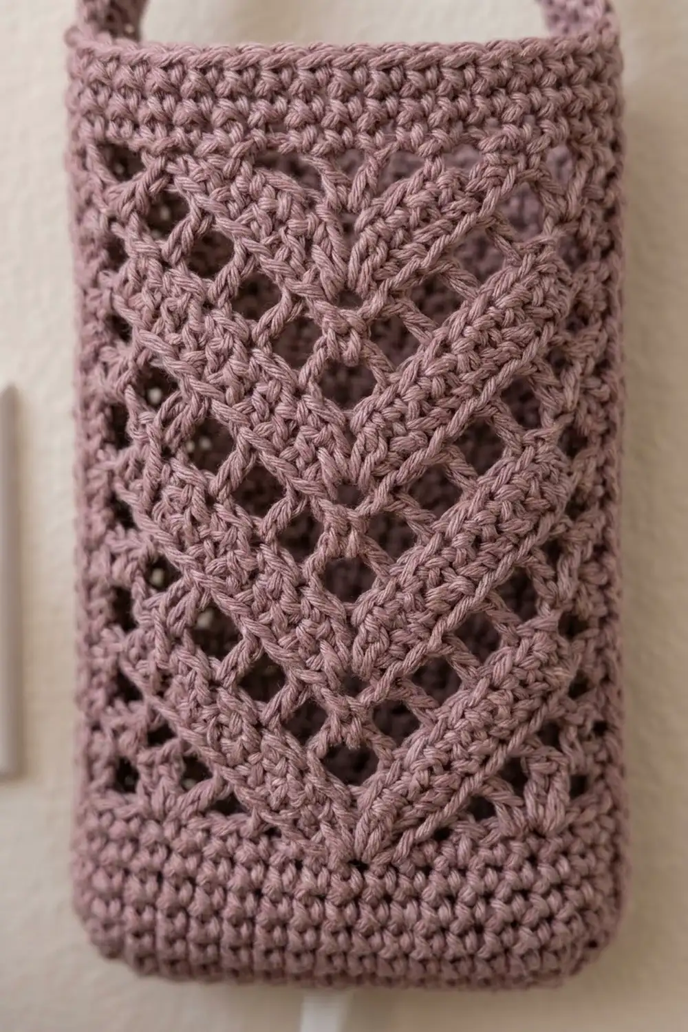 Dusty pink crocheted container with delicate openwork diamond pattern and visible yarn texture detail on neutral background.