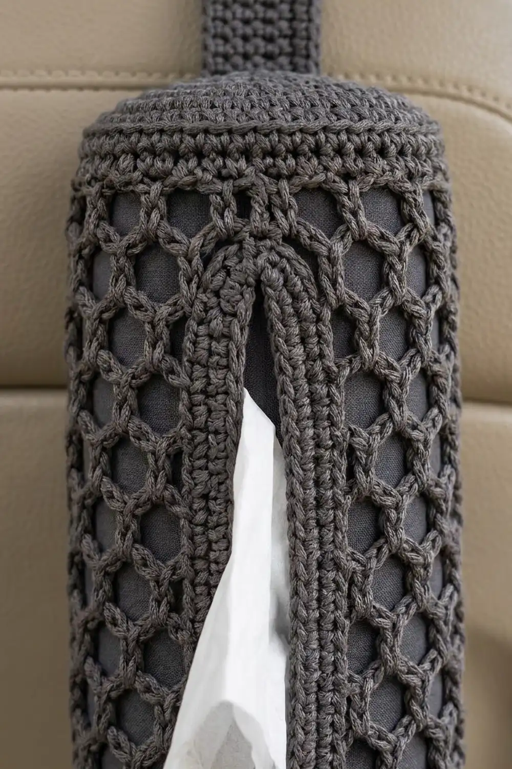 Close-up of gray crocheted fabric with open lattice pattern and braided cable details, photographed against a neutral beige background.