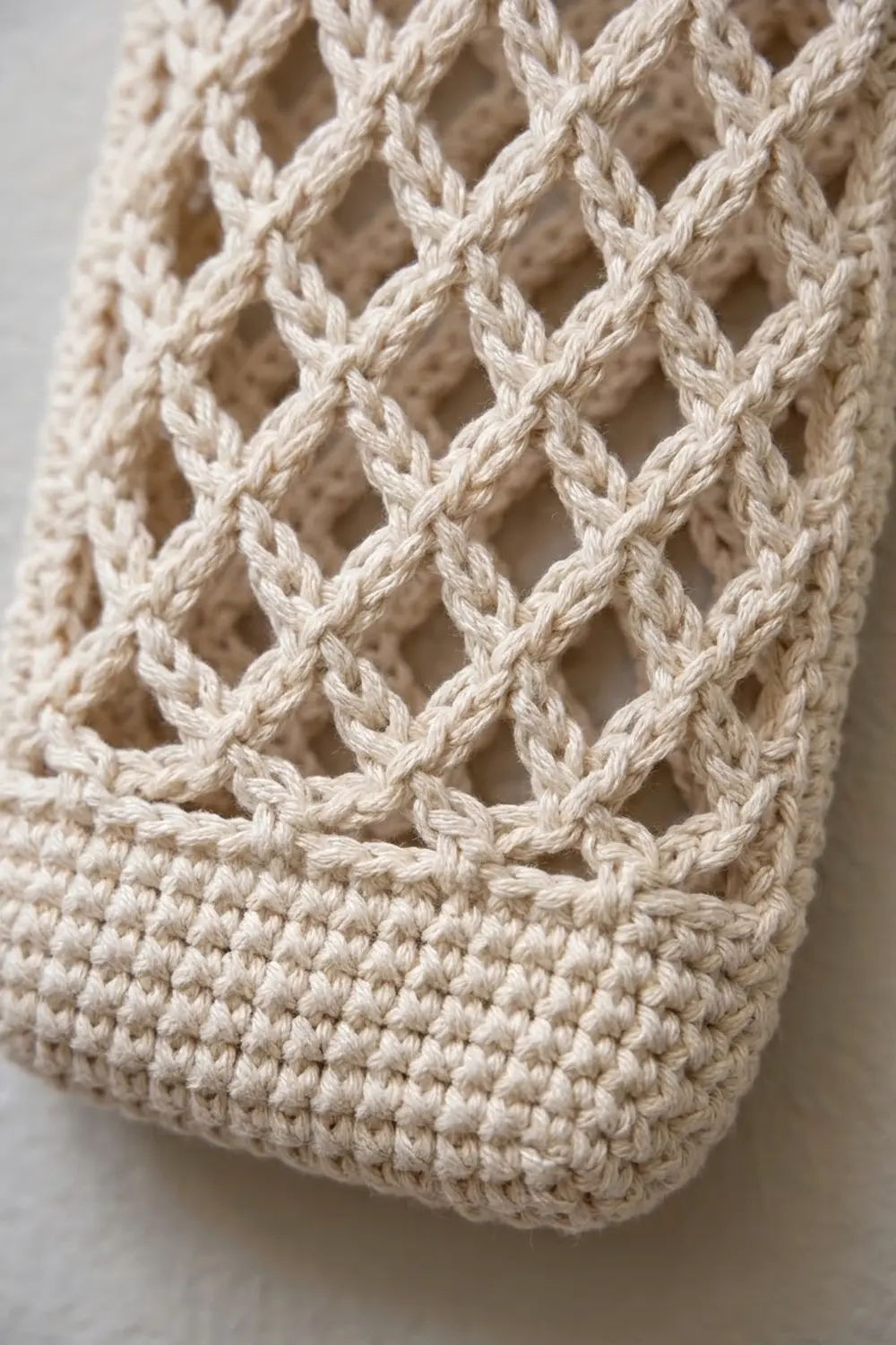 Cream-colored crochet fabric with openwork diamond lattice pattern and dense textured base stitch.