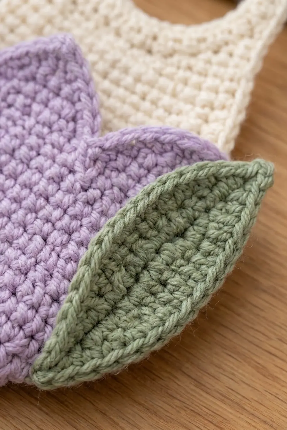 Lavender and sage-green crocheted leaves with cream crochet in background, displayed on light wood surface.