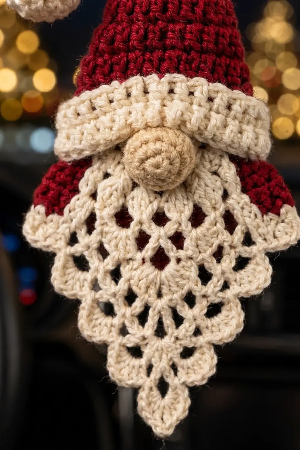 Cream crocheted beard with lacy open-work design against a red knit hat with golden bokeh lights behind.