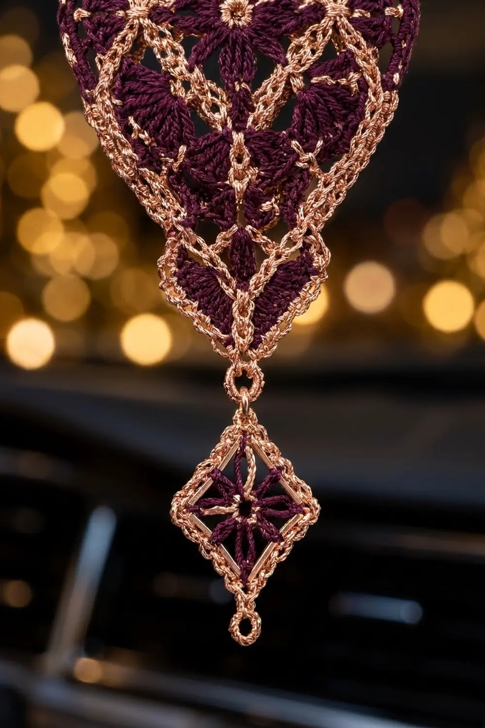 Crocheted pendant in deep purple and gold with geometric lattice pattern, photographed against warm bokeh lights.