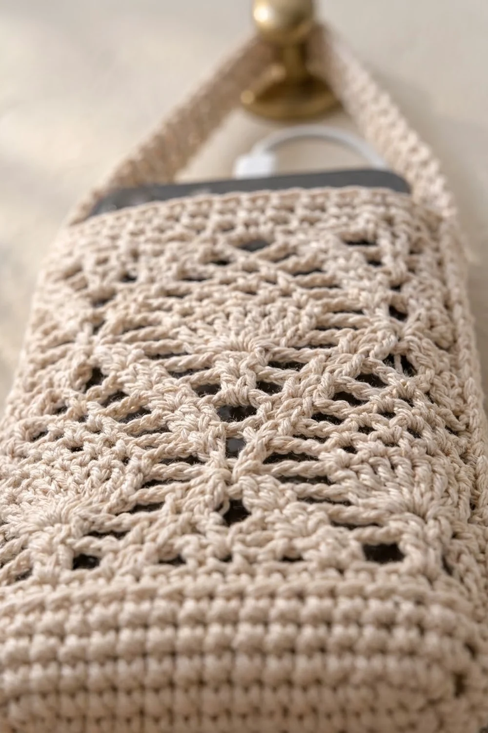 Cream crocheted lace shawl with openwork pattern and dark striped band, hanging from a decorative brass finial hook.