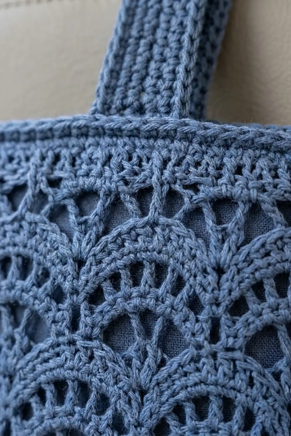 Close-up of a blue crocheted tote with intricate lacework pattern, showing detailed stitching and geometric openings against a neutral background.