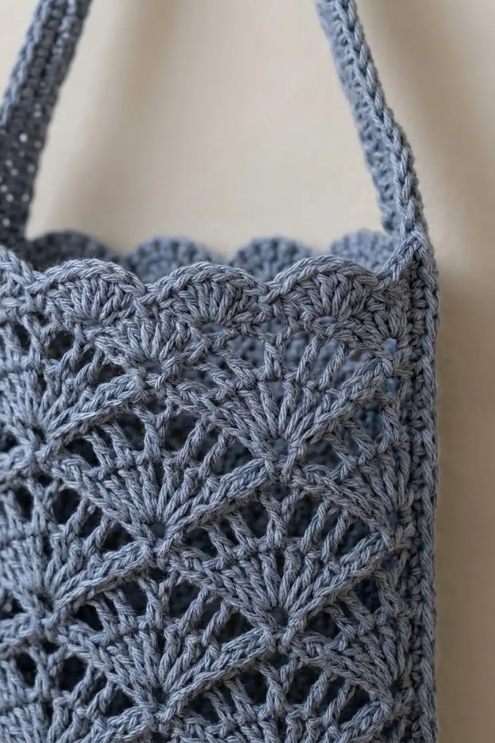 Close-up of a light blue crocheted tote with an intricate openwork diamond stitch pattern and rope handles.