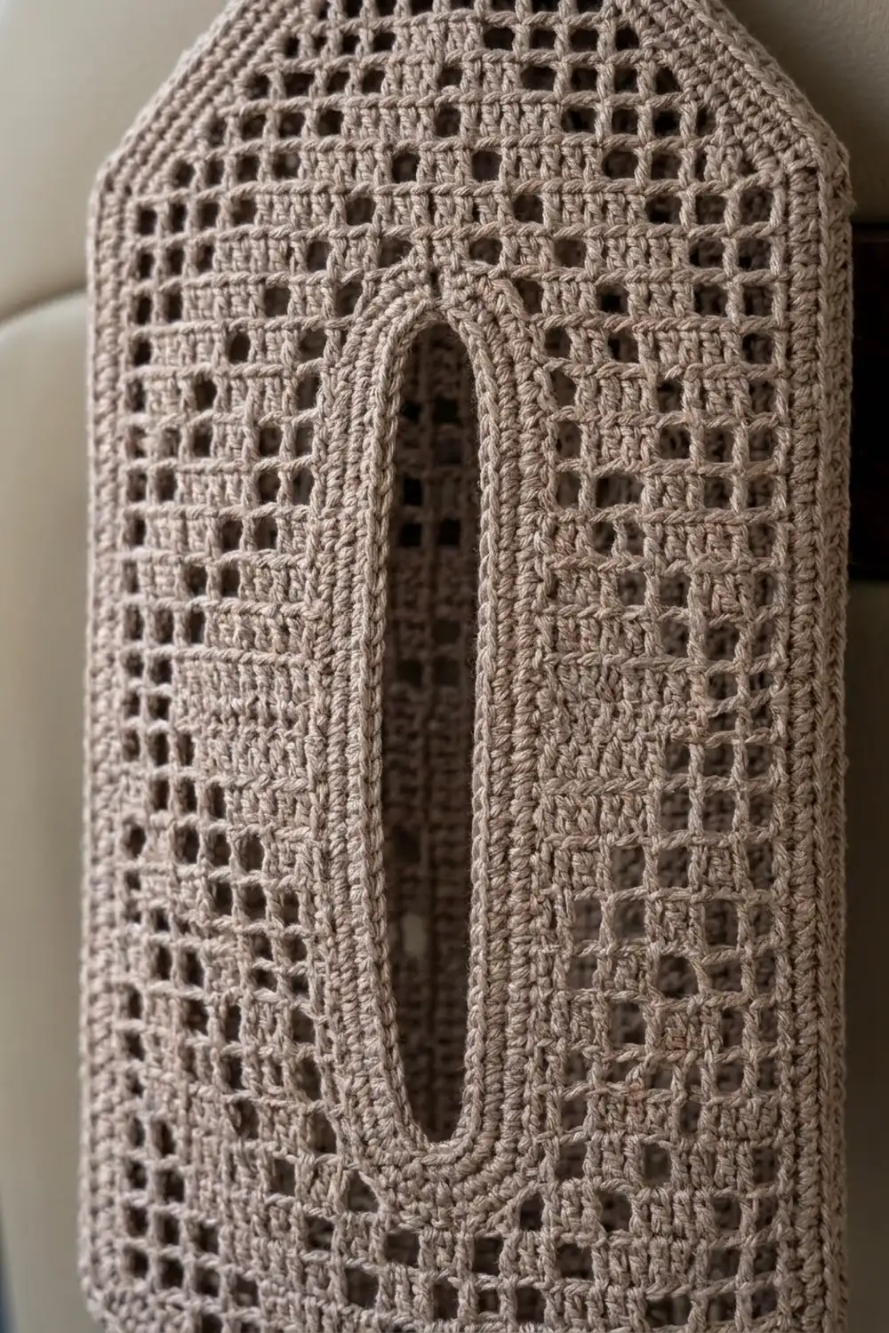 Beige crochet fabric with open lacework pattern and central oval opening, showcasing detailed stitchwork against a soft background.