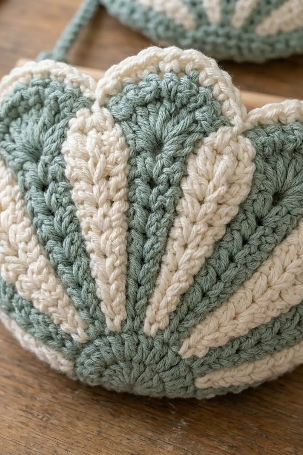 Crocheted fabric showing alternating sage green and cream vertical stripes with visible stitch texture on wood surface.