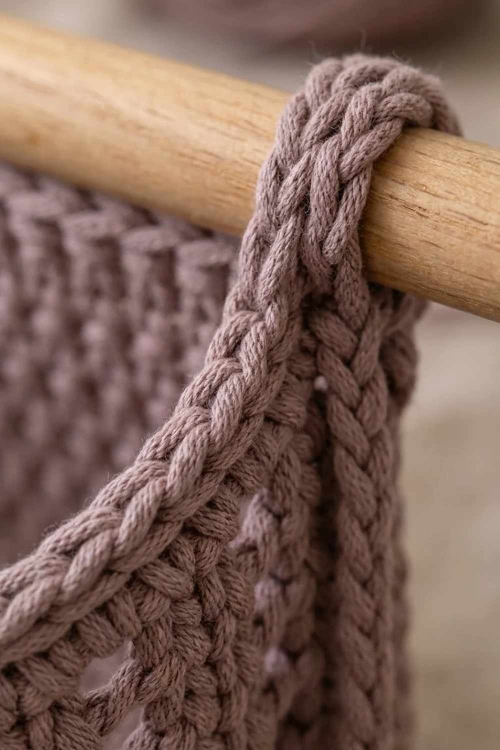 Close-up of taupe crochet blanket with detailed cable pattern hanging from a wooden rod.