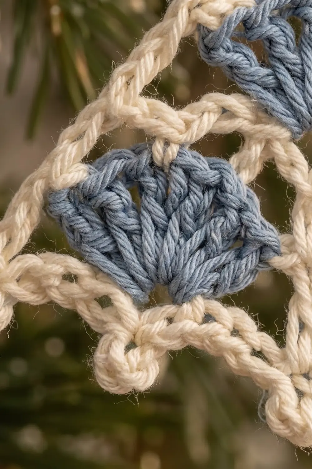 Close-up of a blue knot tied between cream and gray twisted rope strands outdoors.