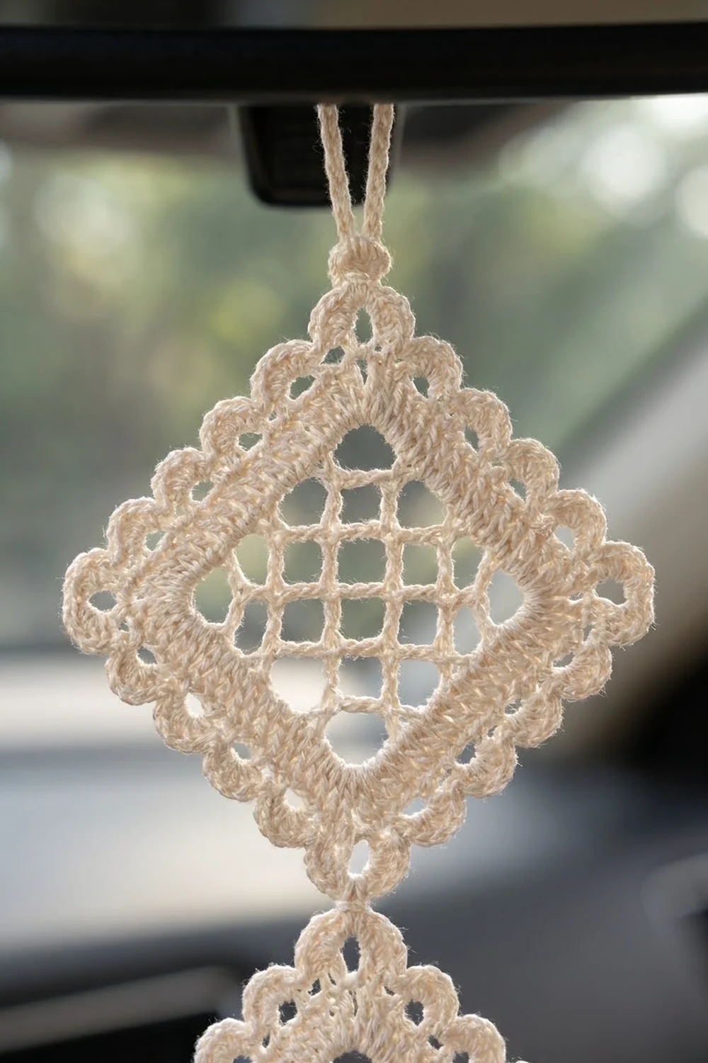 A cream-colored crocheted ornament with delicate geometric openwork pattern hangs against a blurred interior.