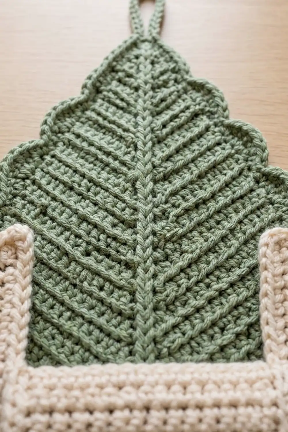 Handmade sage green crochet handbag with intricate herringbone stitch, cream edging, displayed on neutral wood background.