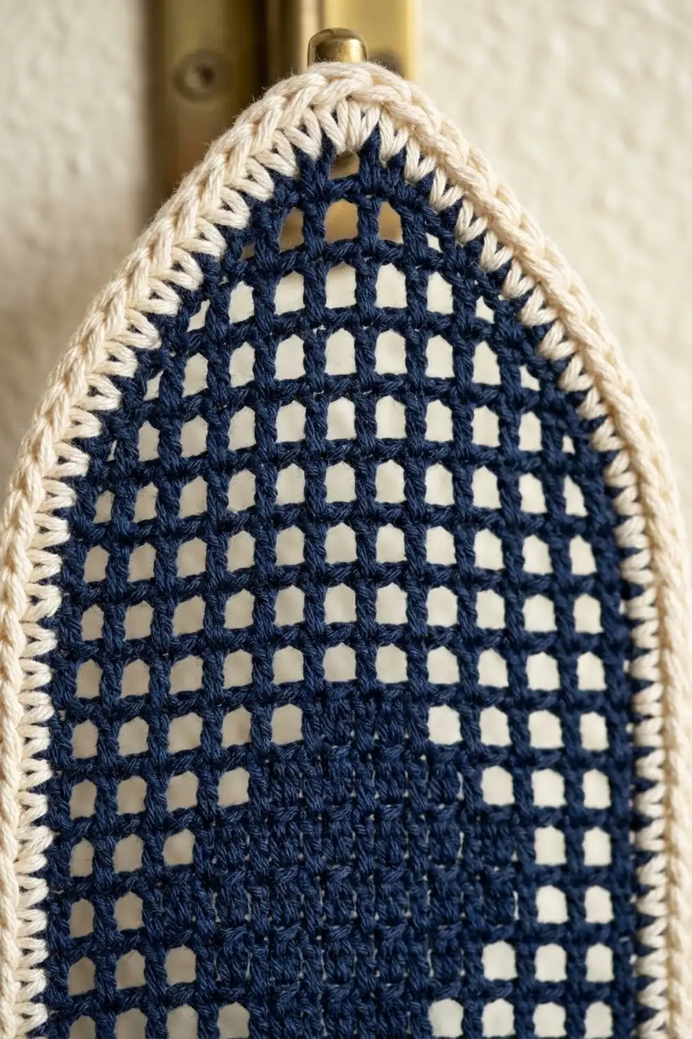 Close-up of a navy mesh and cream crocheted teardrop ornament with gold cap and scalloped edge trim.
