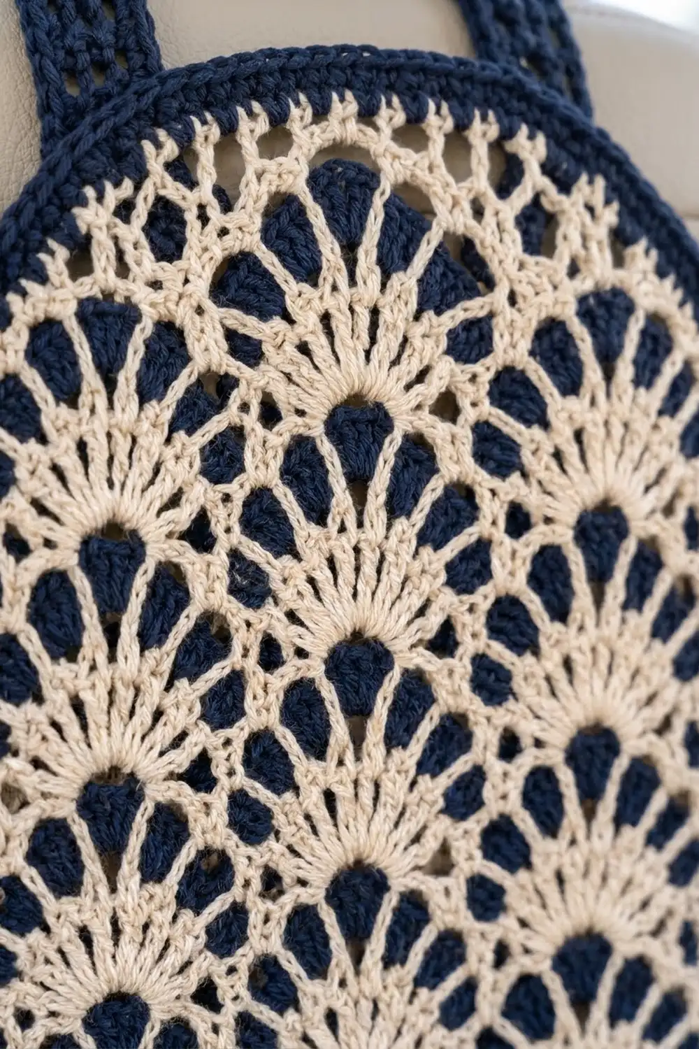 Close-up of a navy and cream crocheted tote bag featuring an intricate lace pattern with floral-like motifs throughout the fabric.