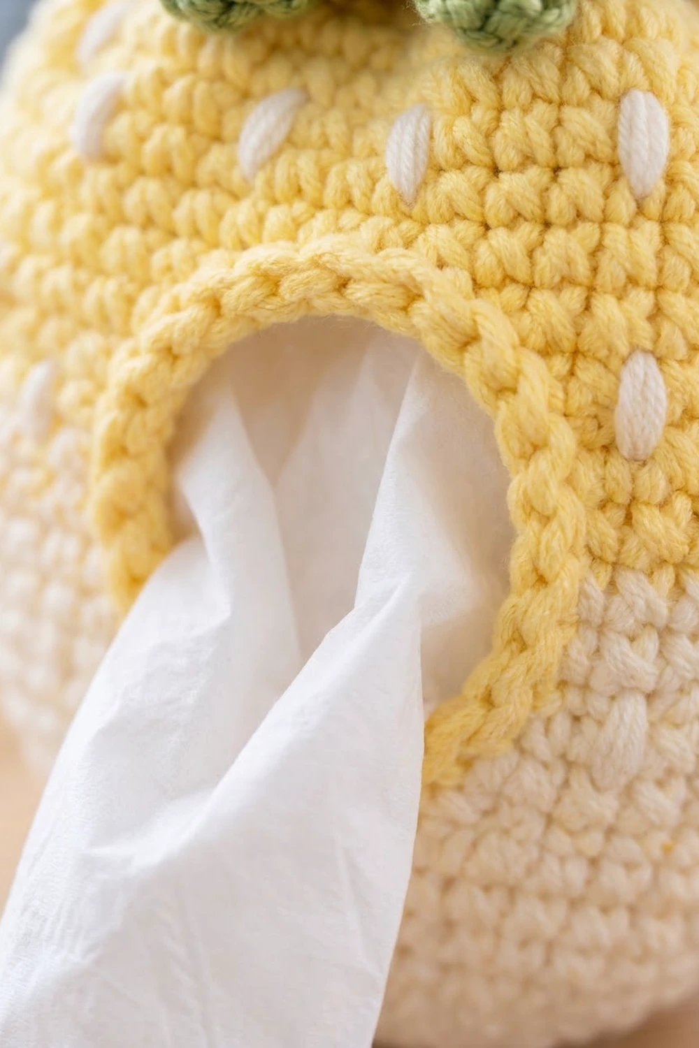 Close-up of pale yellow crochet with white embroidered eyes and stitched mouth on a handmade stuffed toy.