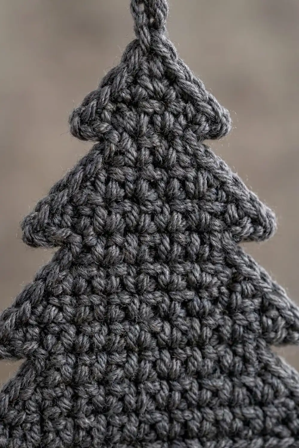 Close-up of a gray crocheted Christmas tree ornament displaying dense bobble stitch texture against a neutral background.