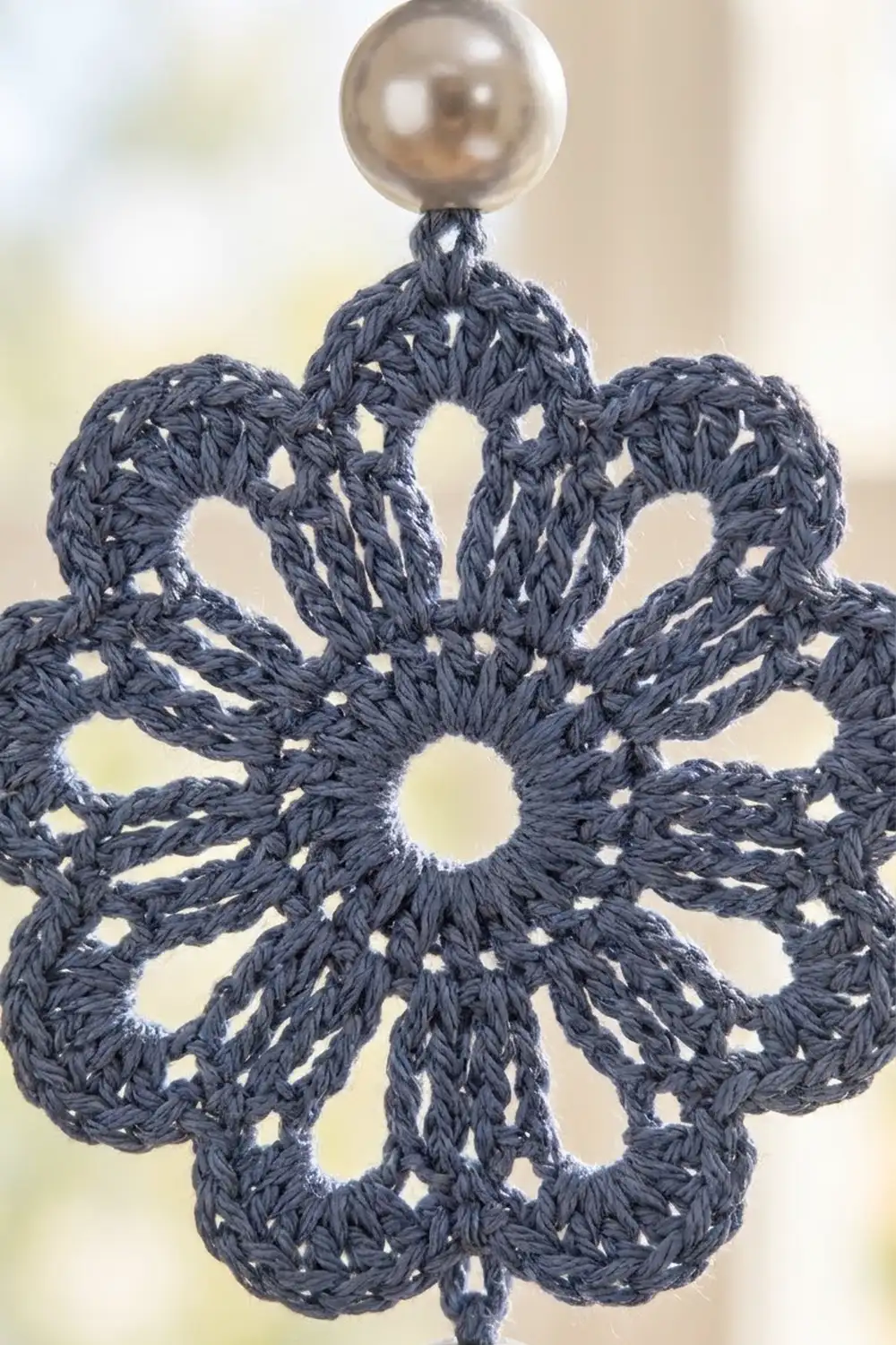 Intricate navy crocheted snowflake ornament with silver metallic bead top against softly blurred background.