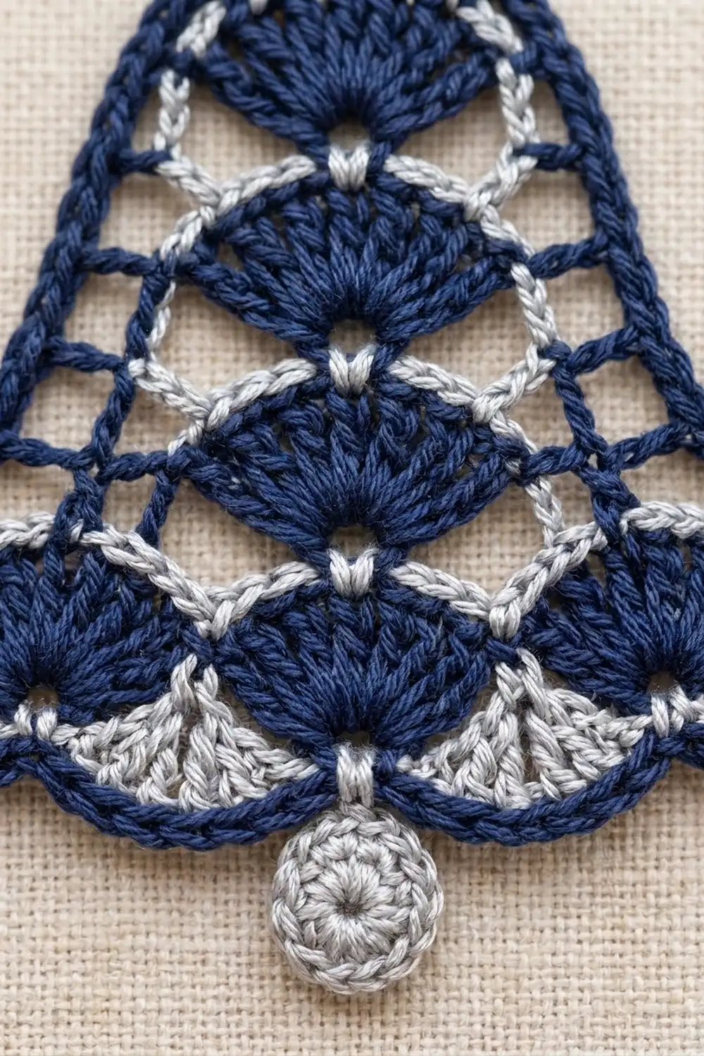 Close-up of navy blue and gray crochet lace trim with shell stitches and a small pendant ornament.