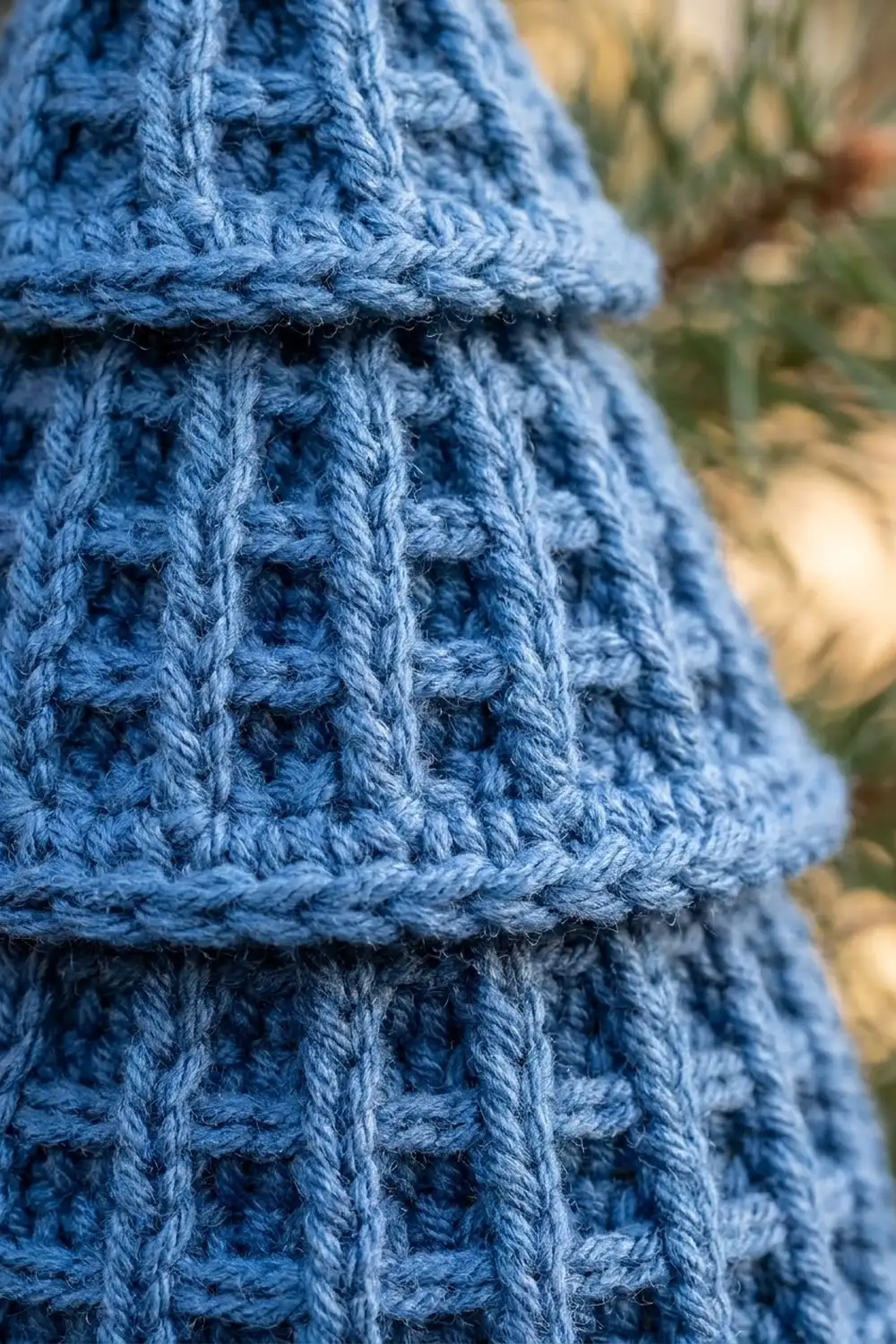 Detailed blue crocheted piece displaying waffle texture stitch with dimensional shadows and blurred natural background.