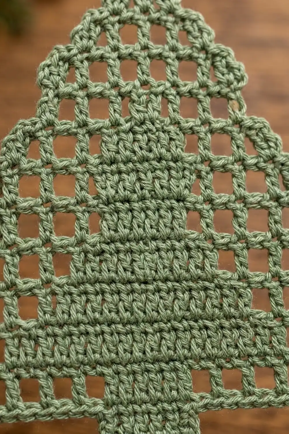 Muted green crochet displaying openwork lattice pattern and dense stitched sections with soft brown blurred background.