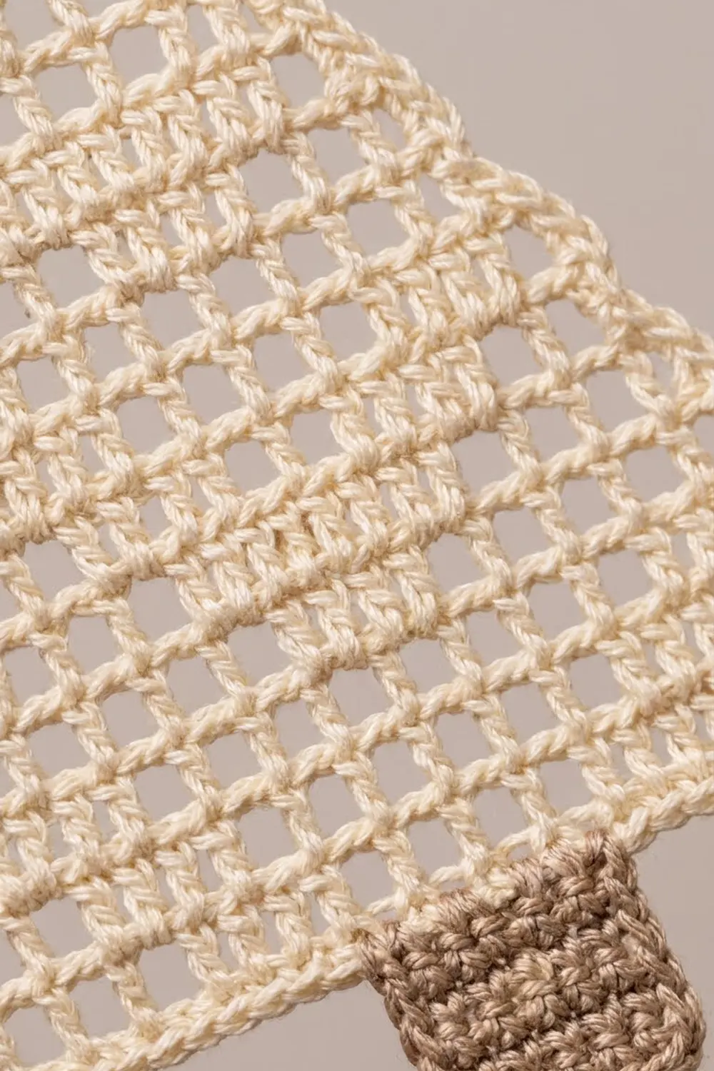 Cream crochet fabric with open mesh pattern transitioning to denser taupe stitching detail on neutral background.
