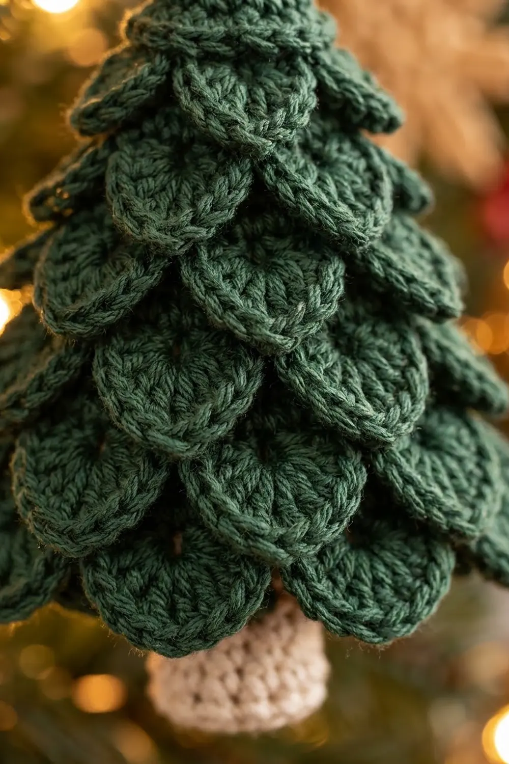 Dark green crocheted pine tree ornament with textured detail and cream-colored base against a warm, blurred golden background.