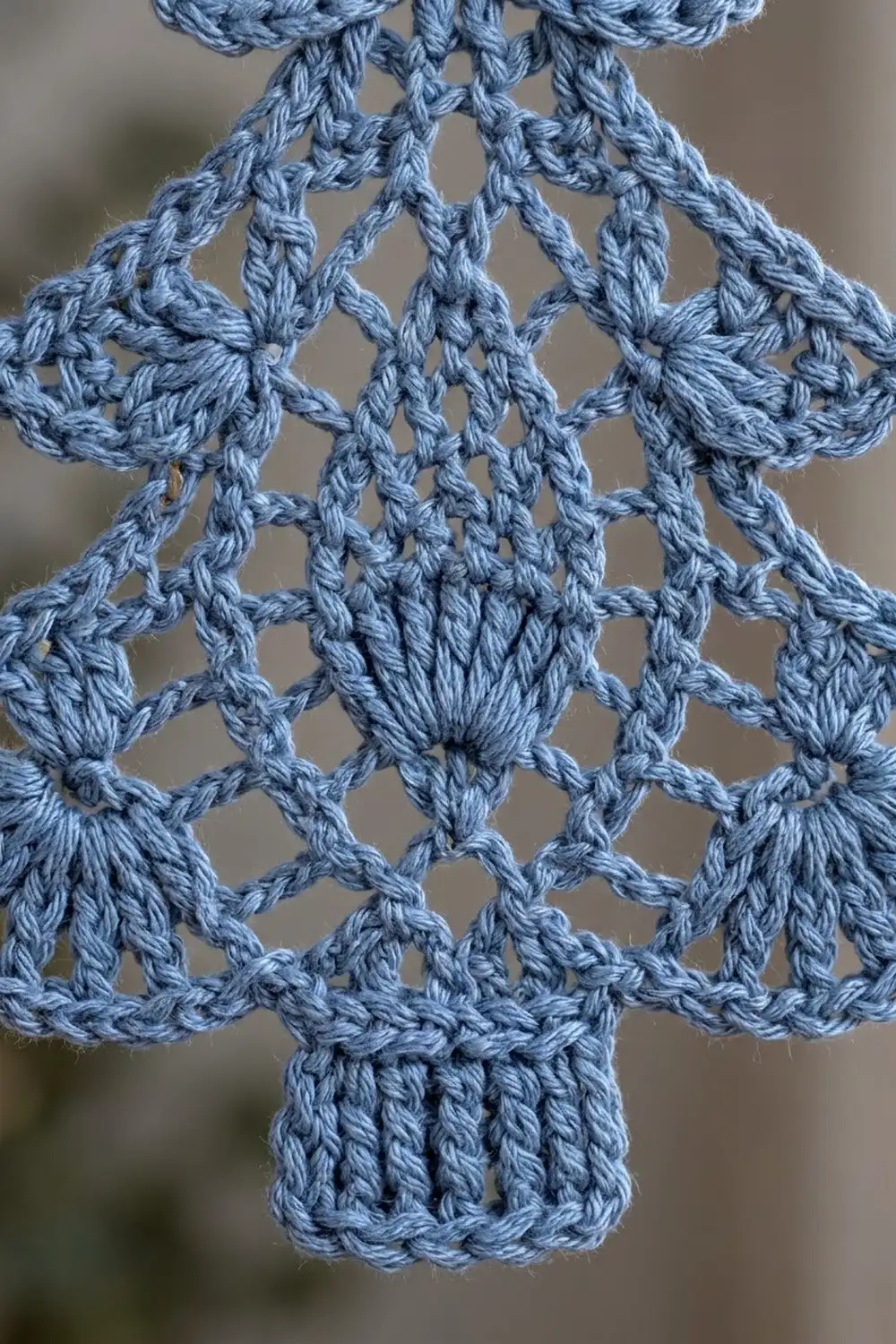 Delicate light blue crocheted lace snowflake with symmetrical star patterns against a soft blurred background.