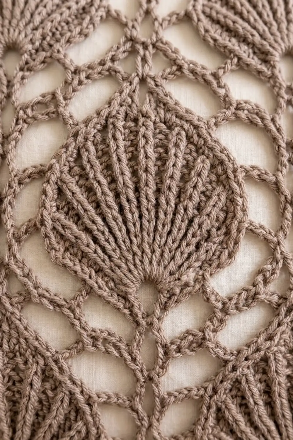 Close-up of beige crocheted textile with geometric open-work pattern and raised textured center motif.