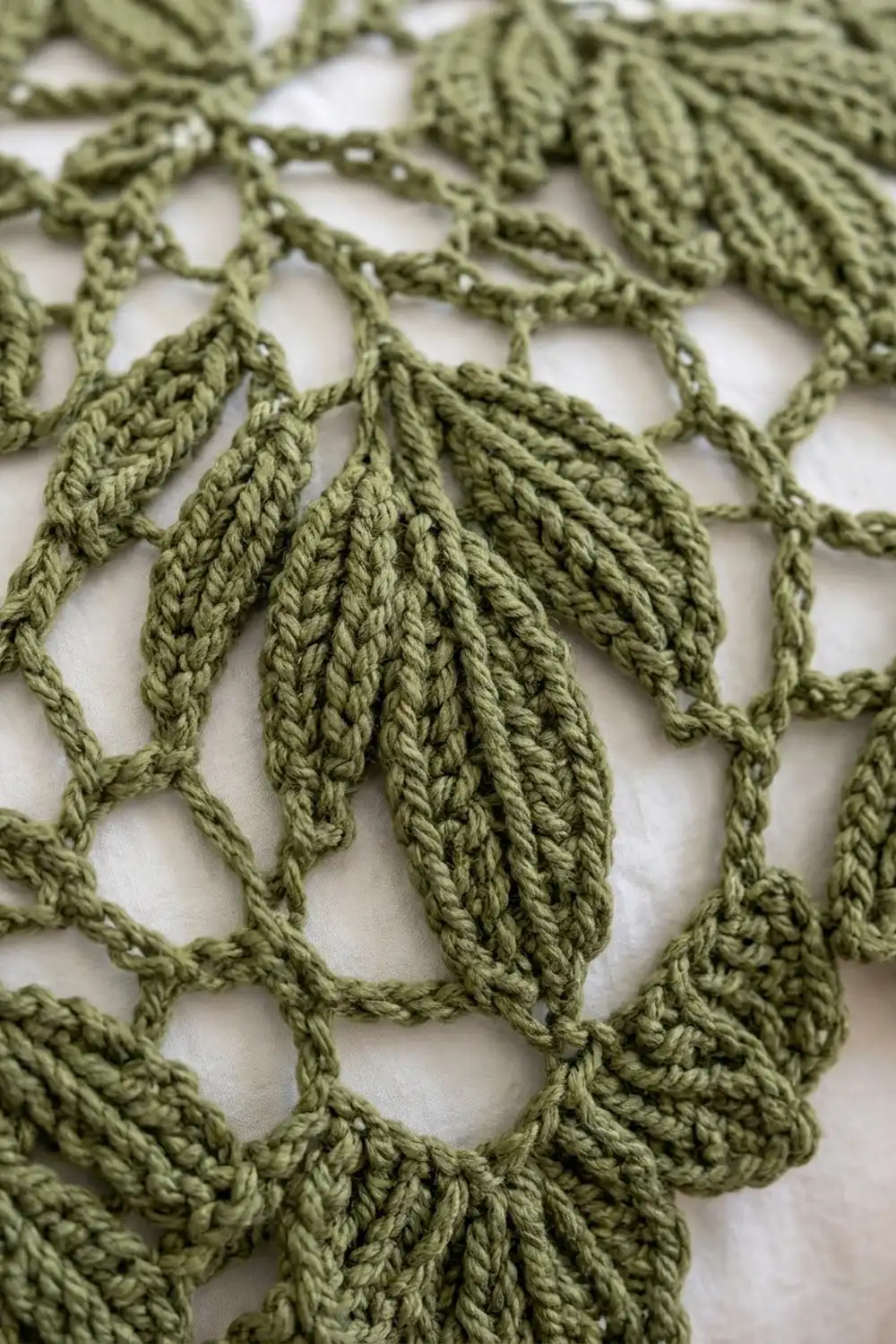 Sage green crocheted lace with delicate leaf motifs and openwork pattern on a white background.