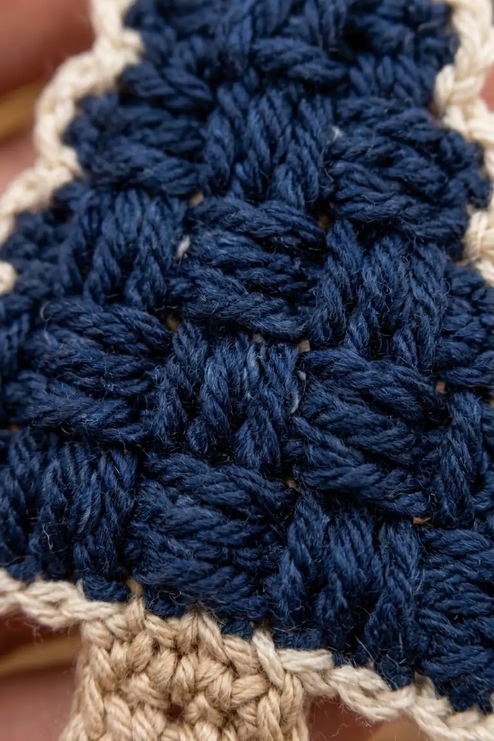 Close-up of navy blue crochet stitches with cream-colored border, showing textured braided pattern detail.