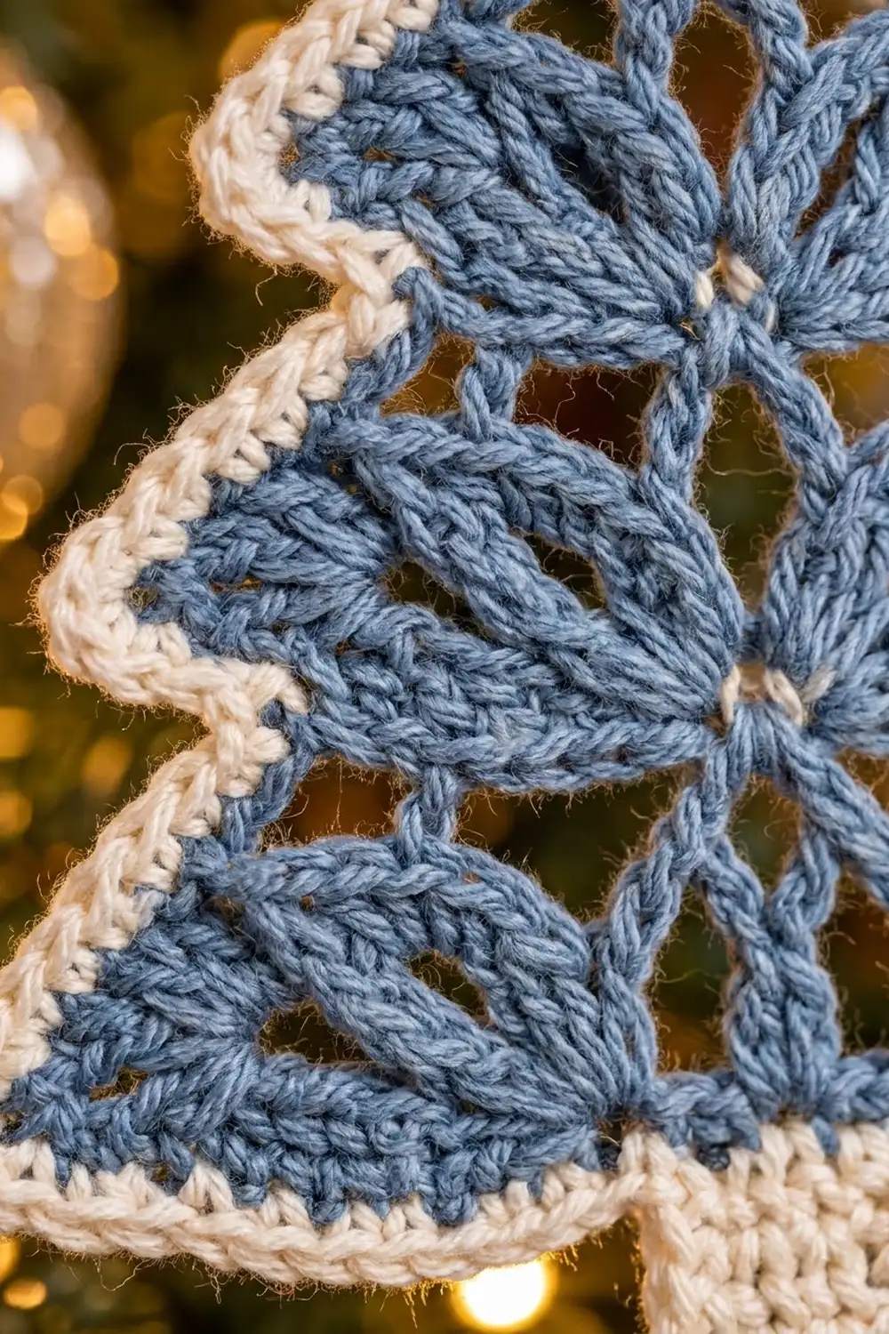 Close-up of interlocking blue and cream crocheted stitches with geometric pattern and blurred golden background.