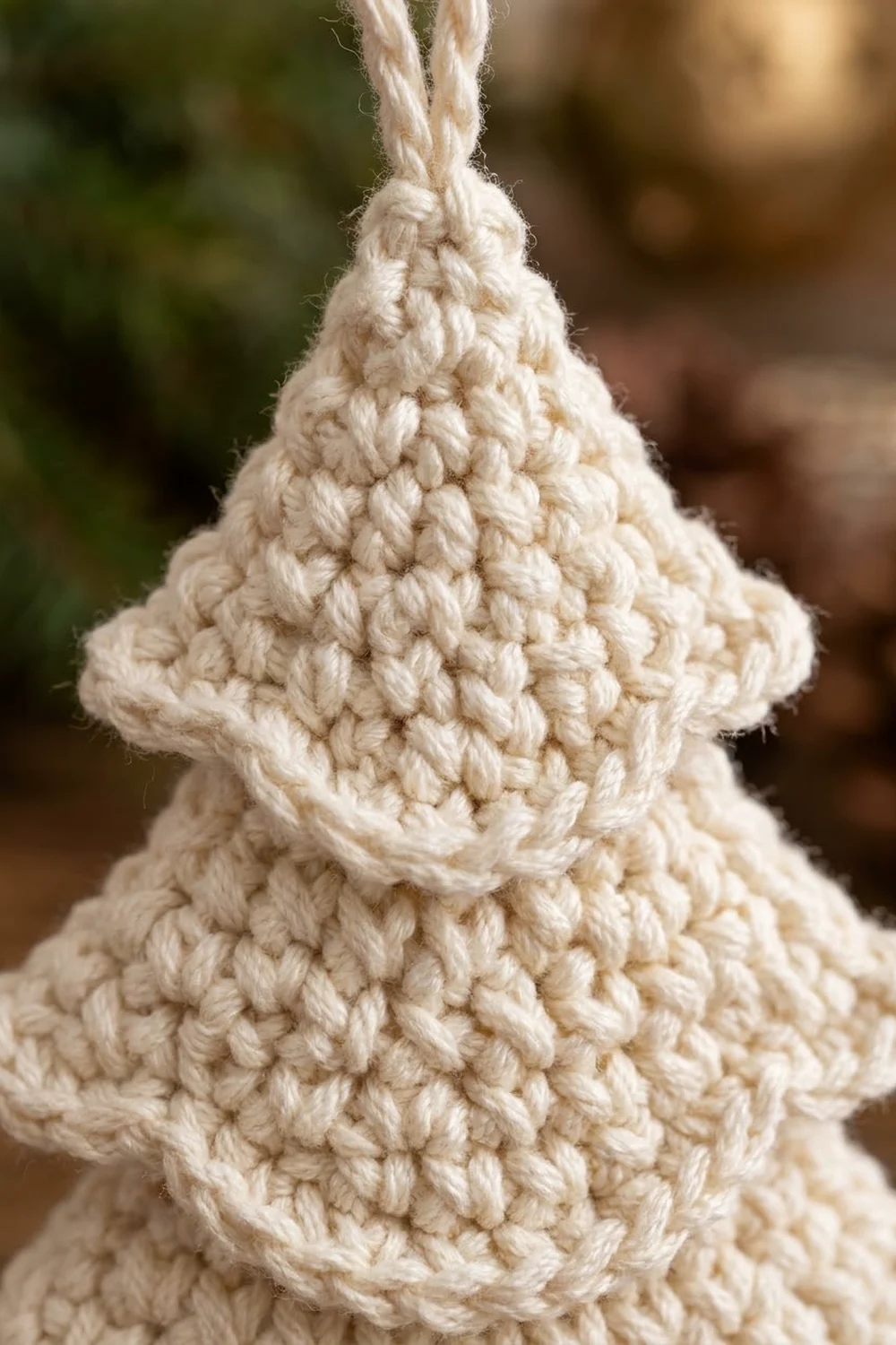 Cream-colored crocheted ornament with textured loop stitches and hanging cord against a blurred outdoor background.
