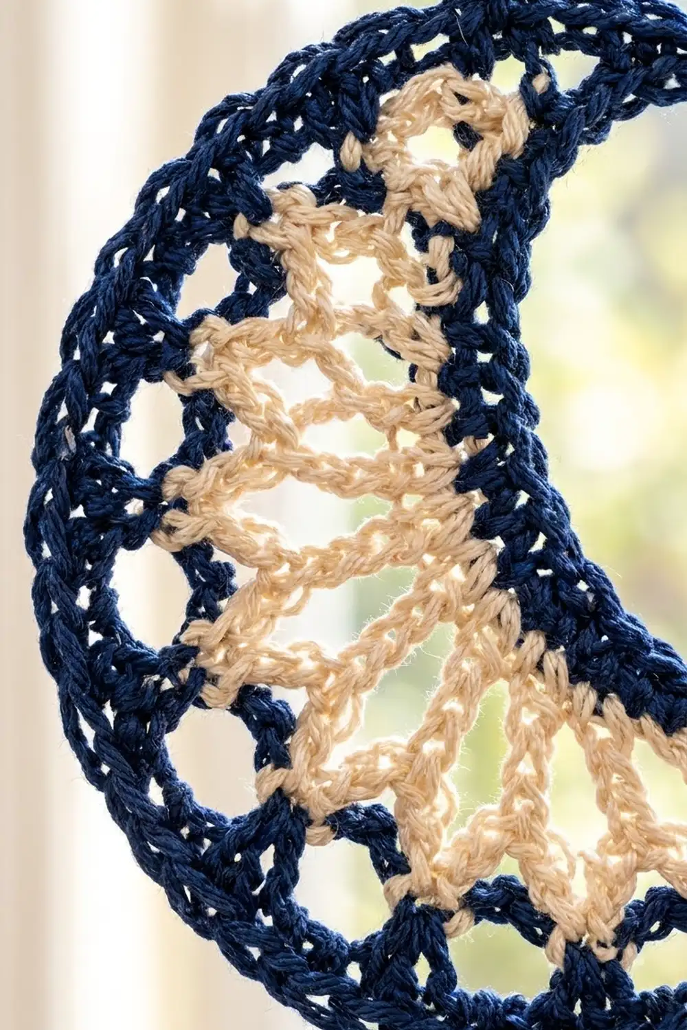Navy and tan crocheted lace with interlocking geometric lattice pattern, held backlit against a soft, blurred background.