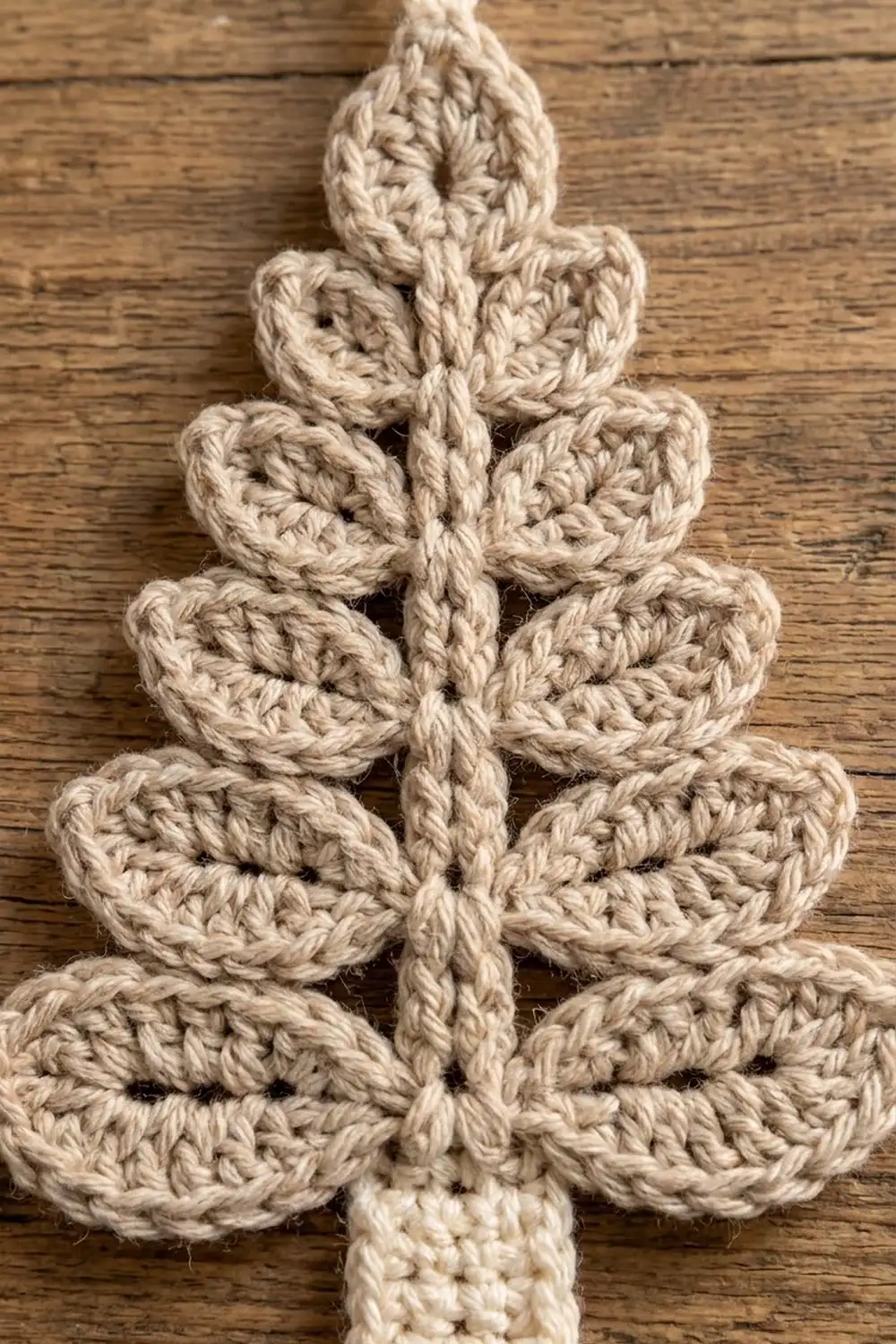 Handmade crocheted Christmas tree in cream yarn with stacked petal shapes on rustic wood.
