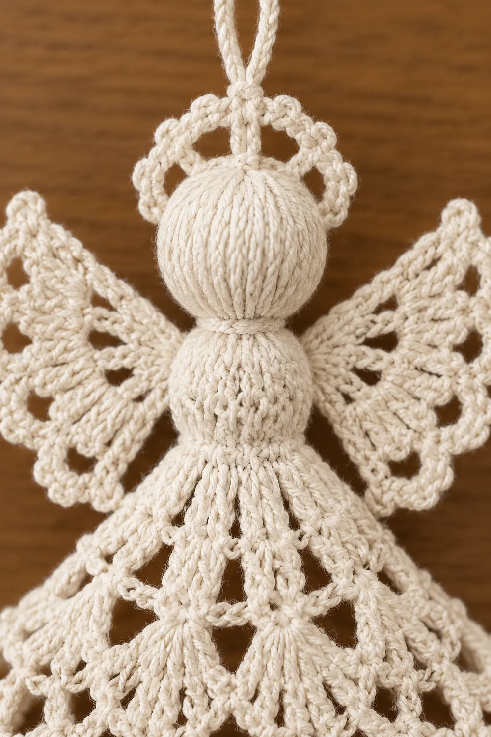 Macramé angel ornament with knotted cream-colored cord body and wings against a wooden background.