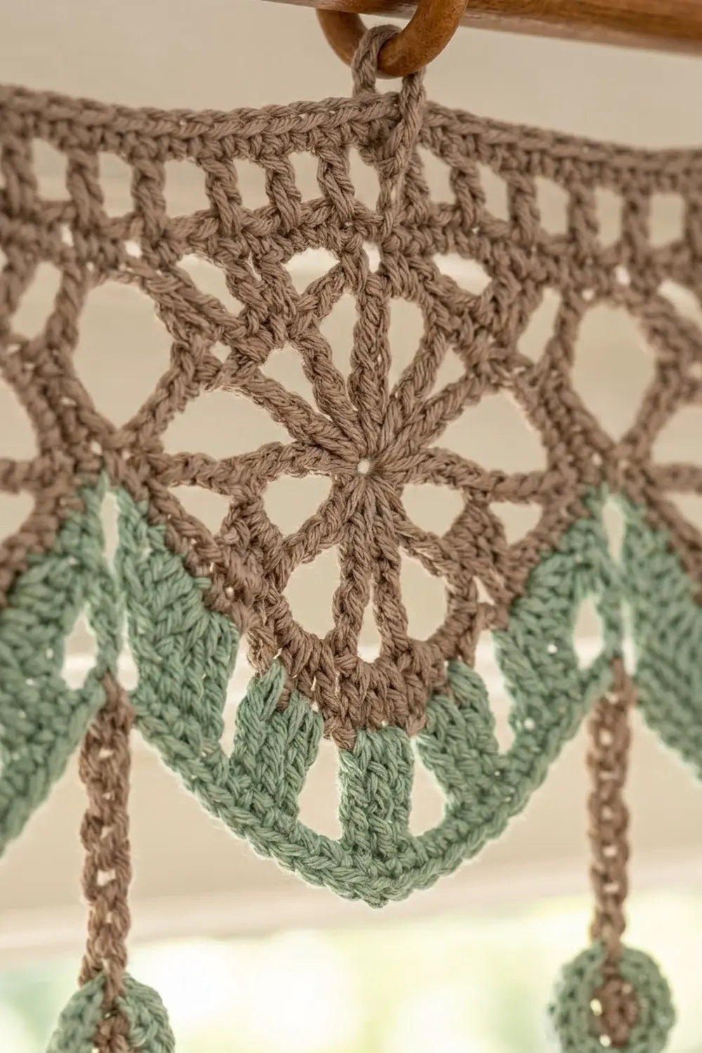 Handmade crochet wall hanging in tan with green details, featuring geometric openwork pattern and hanging beaded trim.