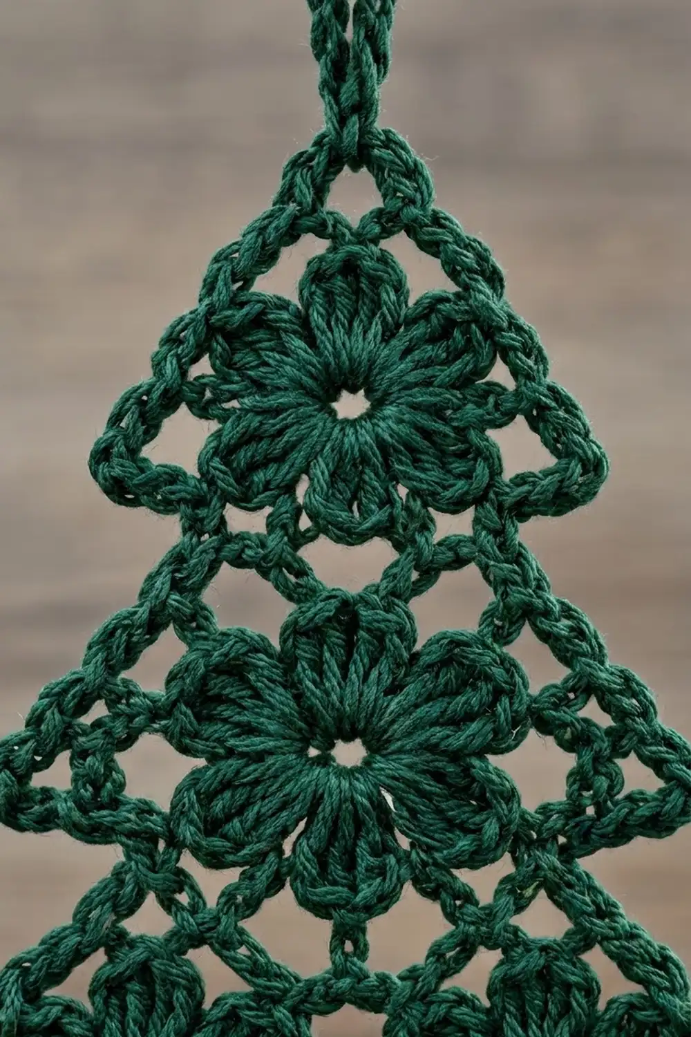 Dark green crocheted Christmas tree ornament with flower motifs against a soft gray background.