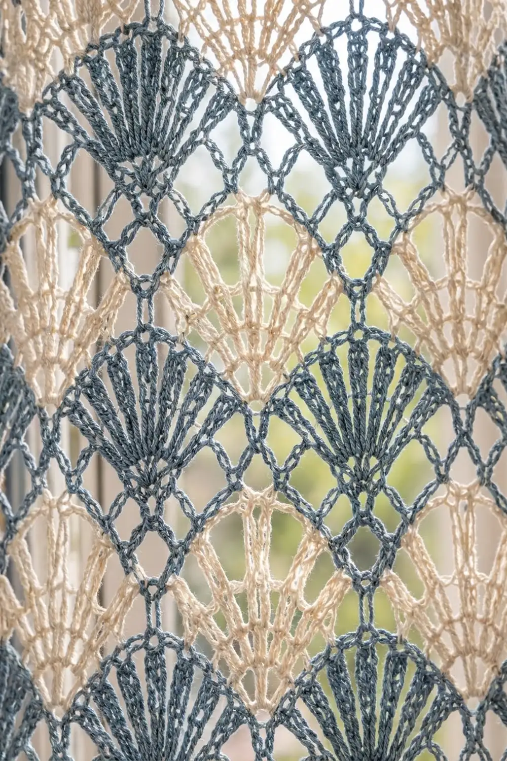 Crocheted lace with dark teal fan motifs and beige lattice work held against diffused outdoor light.