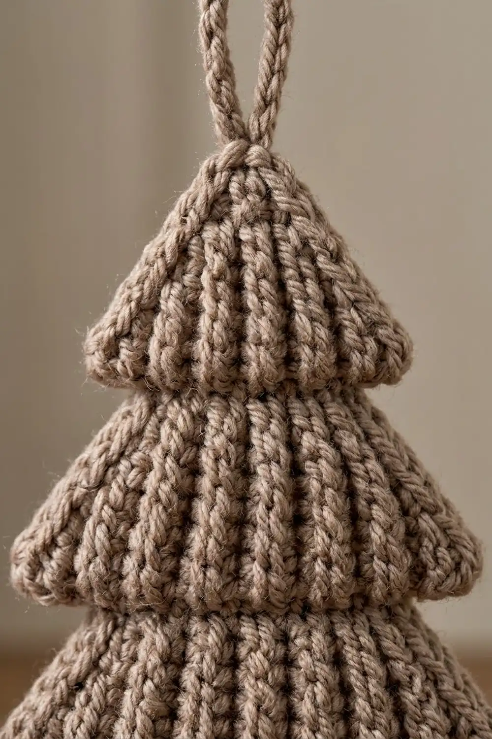 Tan crocheted ornament with braided rope handles against a soft neutral background.